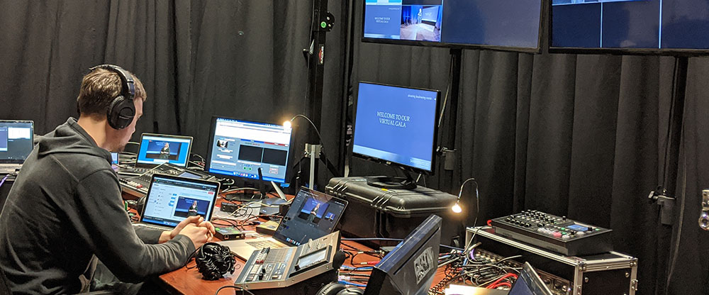 audiovisual technician sits at a tech table while monitoring multiple monitors and laptops