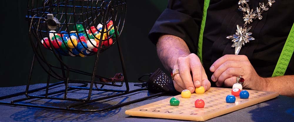 a person calls numbers for a Bingo game and places the numbers on a wooden Bingo board