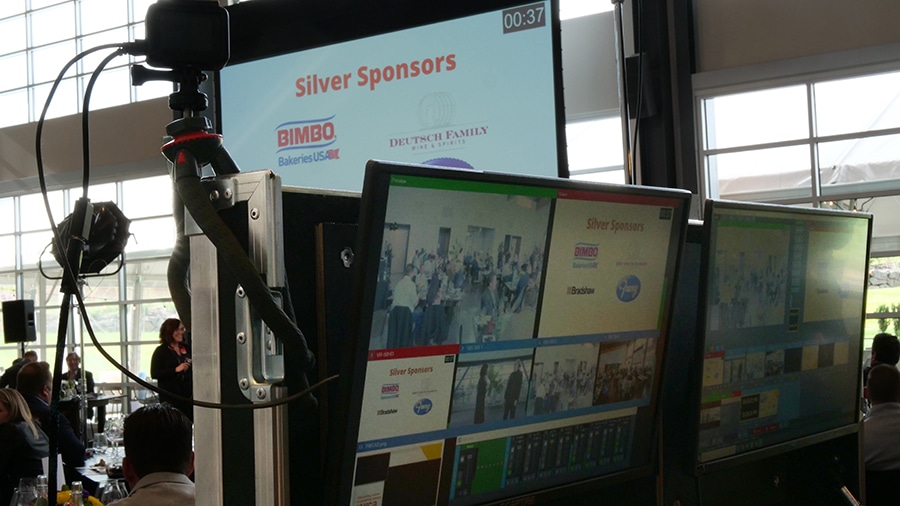 Livestreaming equipment including two monitors is set up for a hybrid event. On the monitors are multiple scenes for the livestream including camera feeds and slide presentations.