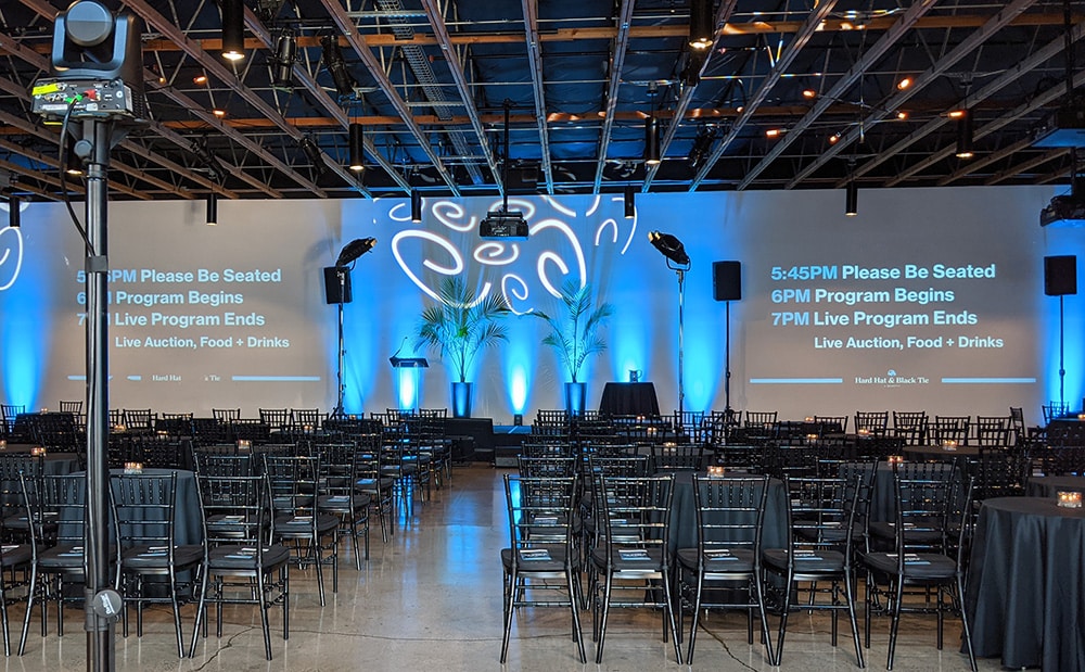 An event venue is set for an audience to watch a live stream of the program. The stage is set with additional lighting and monitors for the hosts.