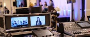 A speaker on the stage is seen in the frame of one of the cameras during a live stream of a hybrid conference