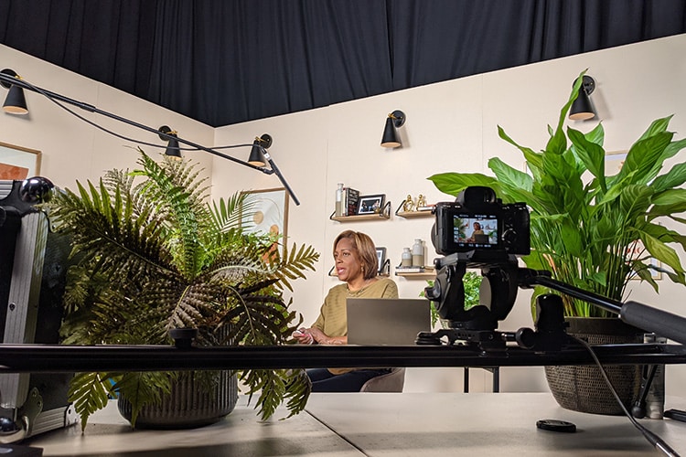 A person films an e-training series in the studio set with a stage that looks like a home office