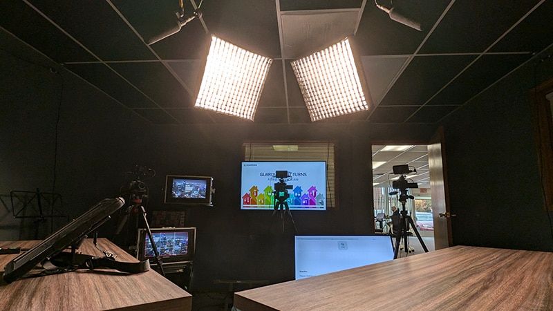 Point of view of a host of a virtual event from The AV Department Production Studio. Lights, microphones, cameras, and multiple monitors are visible.