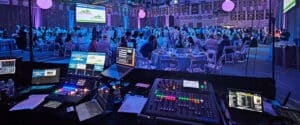 View from the AV tech table. The audio mixing console, computers and monitors are visible during a fundraising gala.